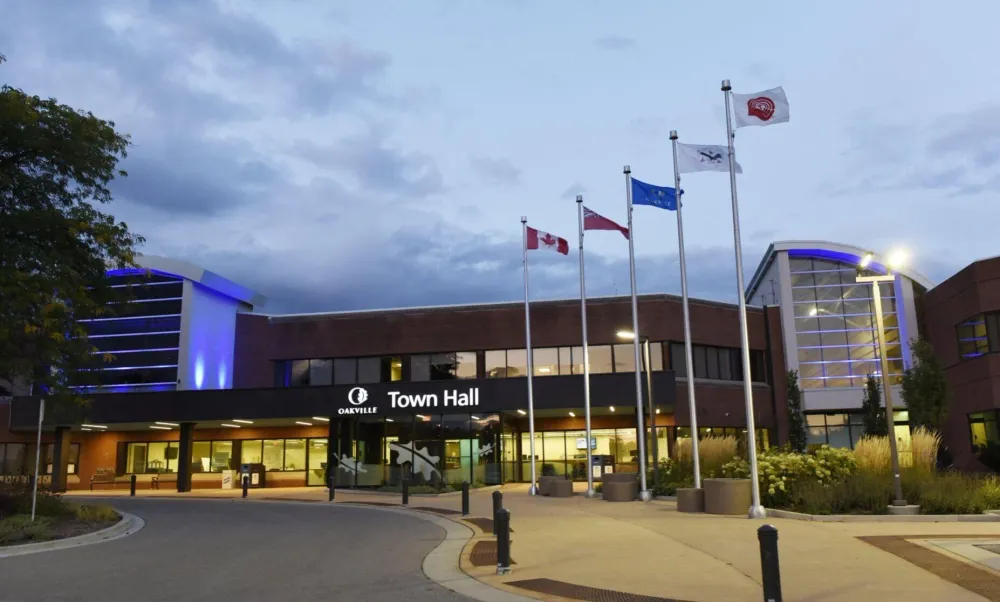 A view of the front of Oakville Town Hall's building. Flag poles are visible and the town's marquee is lit