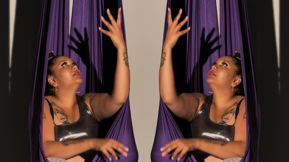 Gaitrie sits in a purple fabric used for aerial swings. The image is mirrored, so you see two Gaitries and two swings.