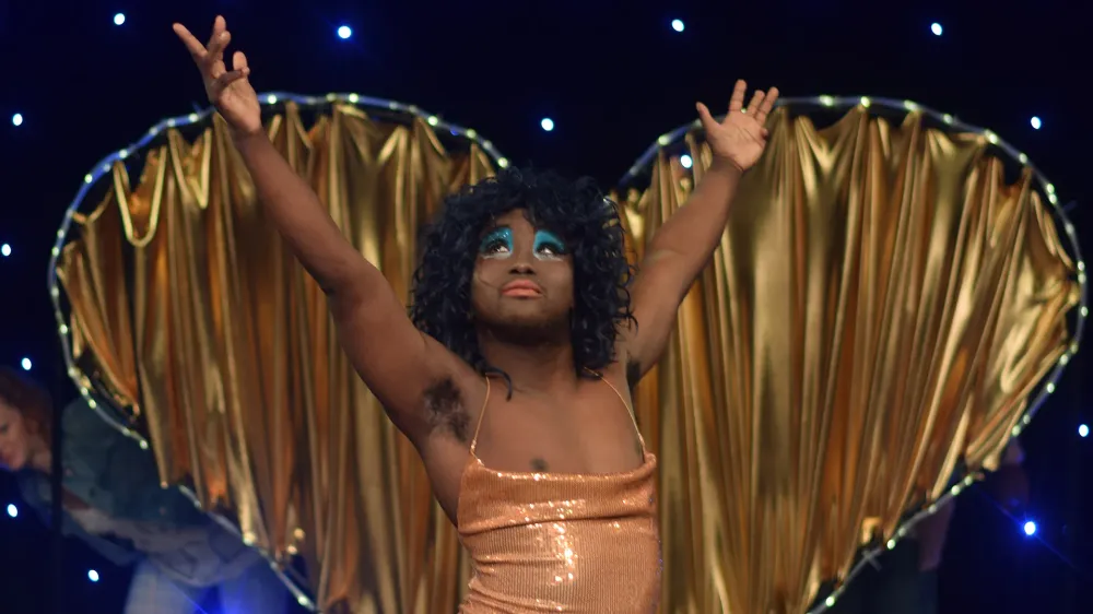 Francis Majekodunmi as Lady Francesca in Girl Meets Boy, wearing a sequinned gold dress and bright blue eyeshadow.