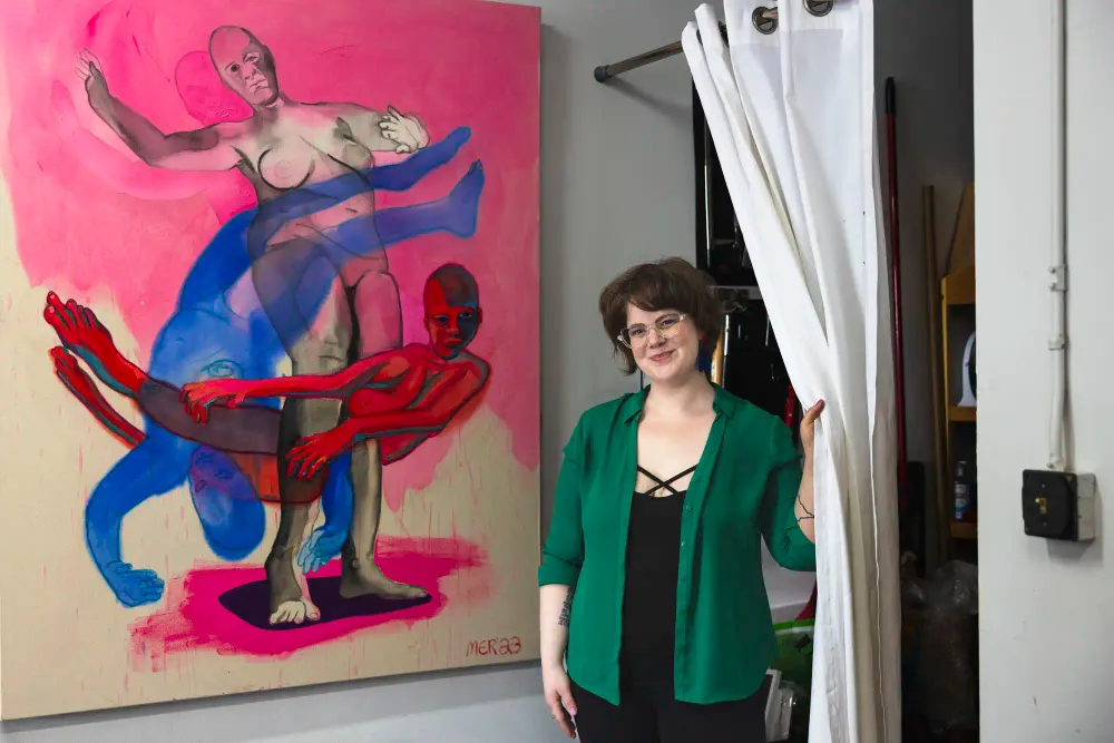 Madison stands next to a giant canvas with three shadowy figures painted on it in white, pink, red, and blue colours.