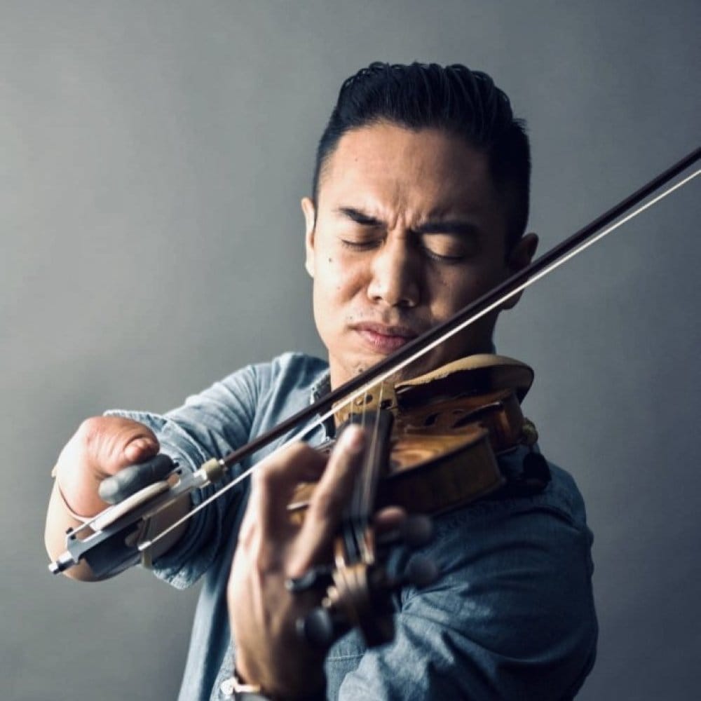 Musician with limb difference playing the violin, their eyes are closed as they concentrate.