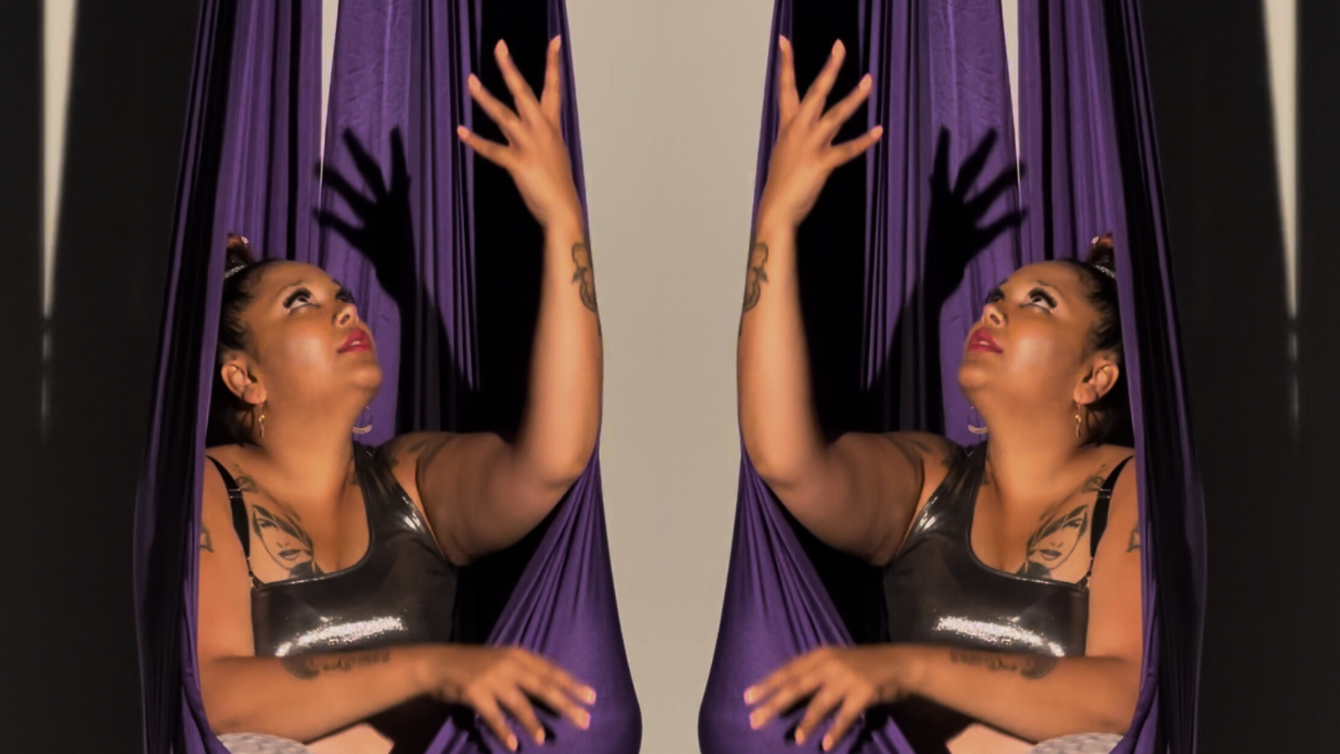 Gaitrie sits in a purple fabric used for aerial swings. The image is mirrored, so you see two Gaitries and two swings.