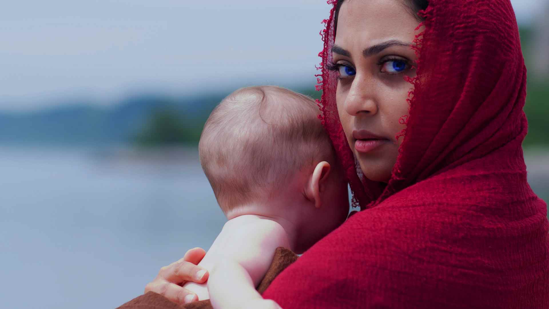 The titular character holds a baby in her arms, water in the background. She looks at the camera with piercing blue eyes.