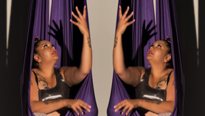 Gaitrie sits in a purple fabric used for aerial swings. The image is mirrored, so you see two Gaitries and two swings.