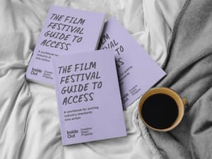 Three purple "The Film Festival Guide to Access" notebooks lay atop a bed with a cup of coffee.